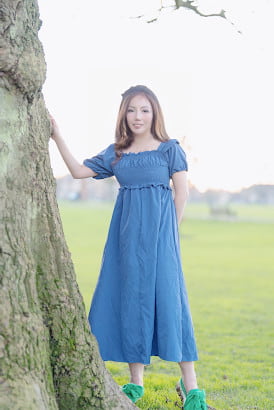 Korean girl in a blue dress with one hand on a mature tree