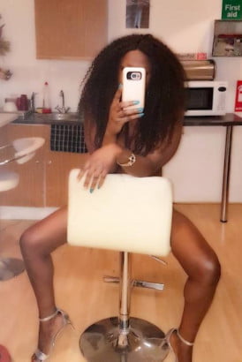 Beautiful black escort taking a selfie whilst sitting on a chair